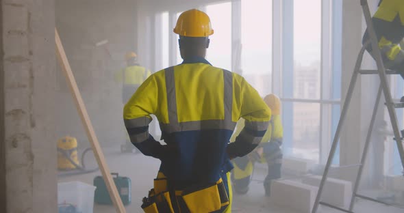 Back View of African Foreman in Uniform Supervising Team of Builders at Construction Site