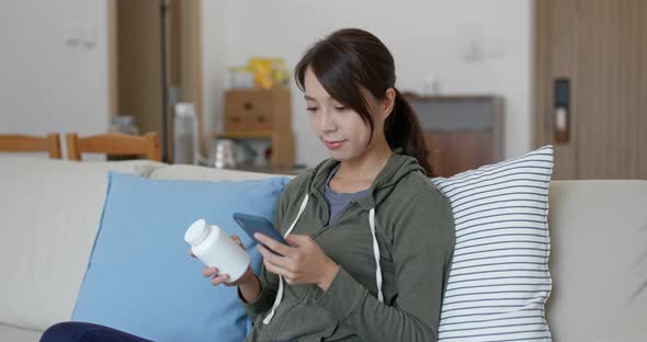 Woman check the ingredients of the bottle of medicine with mobile phone at home