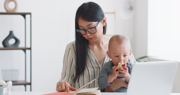 Young Mother Freelancer with Her Child Working at Home Office Using Laptop