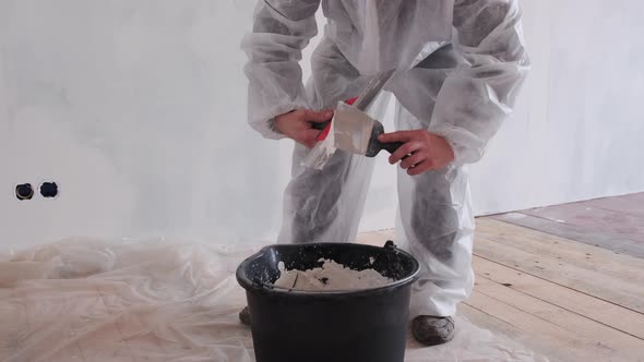 A Man in a Protective Suit Prepares the Plaster for Leveling the Walls