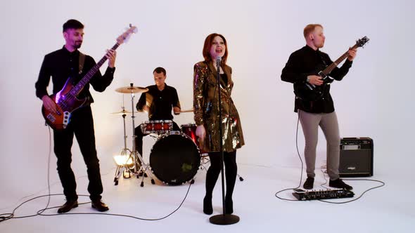 A Musical Band of Four People in Black Clothes Playing Song in the Bright Studio - a Woman Wearing a