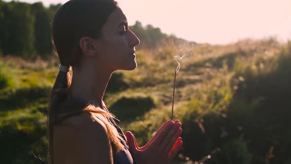 Yoga Woman in Meditate and Breathe on a Sunrise in Nature. Smoke From Aromatic Stick in Hands.