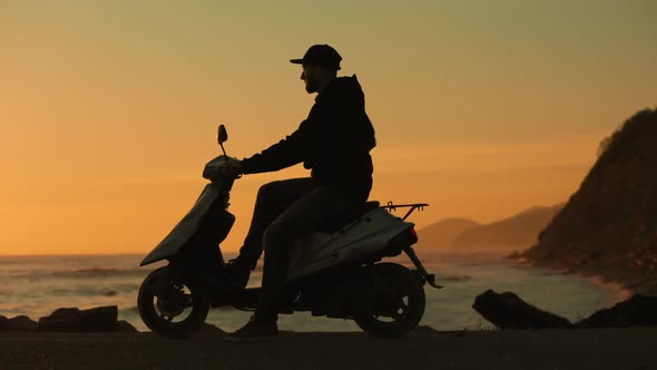 The silhouette of a man who arrived on a moped to the seashore.