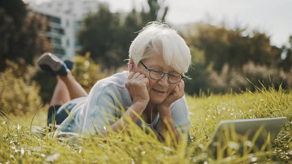 Senior Woman Having a Video Call While Lying on the Autumn Grass in the Park