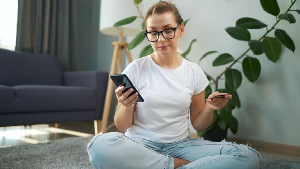 Woman with Glasses is Sitting on the Floor and Makes an Online Purchase Using a Credit Card and