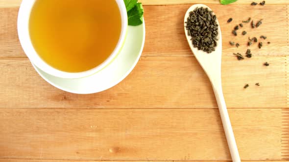 Close-up of tea cup, mint leaves, wooden spoon, dry tea leaves