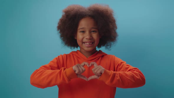 Smiling African American girl making heart shape with fingers looking at camera.