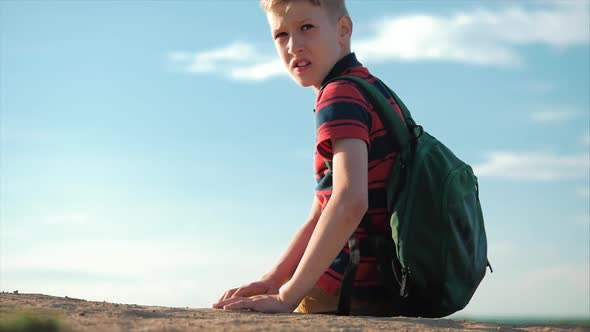 Teenager in a Red Shirt with a Backpack Behind Him, at Sunset, Sitting on a High Hill, Enjoying