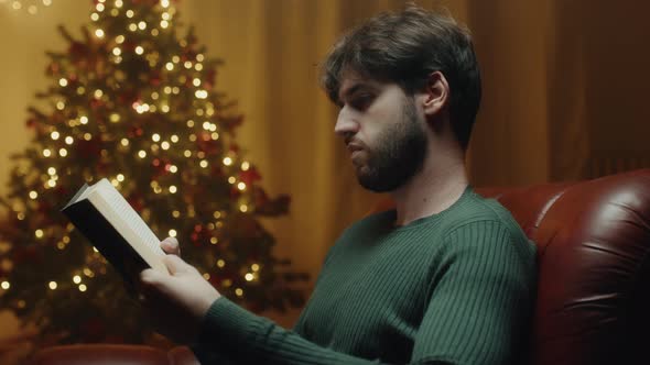 Boy reads book beside Christmas tree