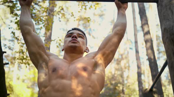 Man is doing pull ups exercises on horizontal bar in the forest gym, outdoors
