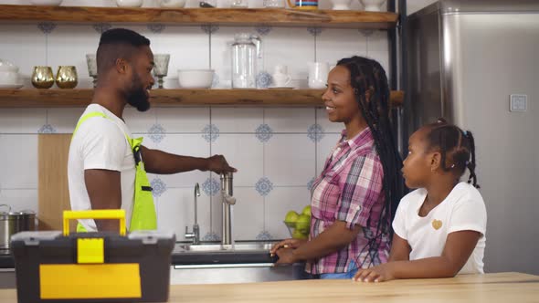 African Plumber Repairing Running Water for Mother and Daughter