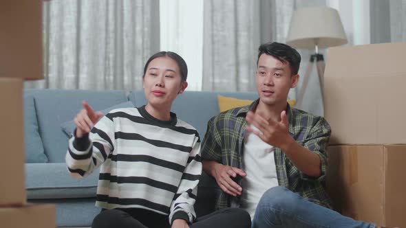 Young Asian Couple With Cardboard Boxes Sit On The Floor And Discuss About The New House