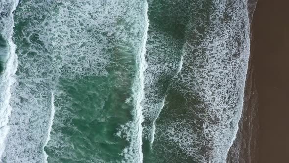 Overheard shot of turquoise waves crashing on a sandy shoreline.