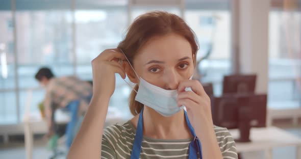 Woman Janitor Putting on Mask Cleaning Modern Office in Business Center