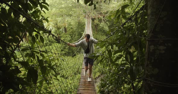 Front Static View of a Man Walking Across a Shaky Rope Jungle Bridge in the Rain Young Man Hanging