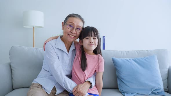 Portrait of Asian elder woman sit with young grandchild in living room and smile, look at camera.