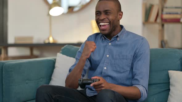 Young African Man Celebrating Success on Video Game on Sofa