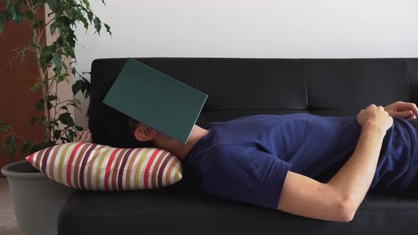 Man lying on the couch sleeping, with his face covered by a book.