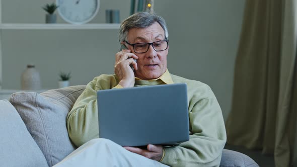 Old Caucasian Grandfather Aged 60s Man Senior Male with Laptop Sits on Sofa at Home Talking on