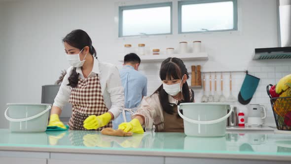 Asian young family wearing face mask due to Covid and teaching their daughter clean kitchen counter