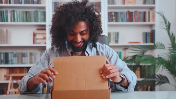 Overjoyed Young Middle Eastern Man Engaged in Unpacking Cardbox with Goods