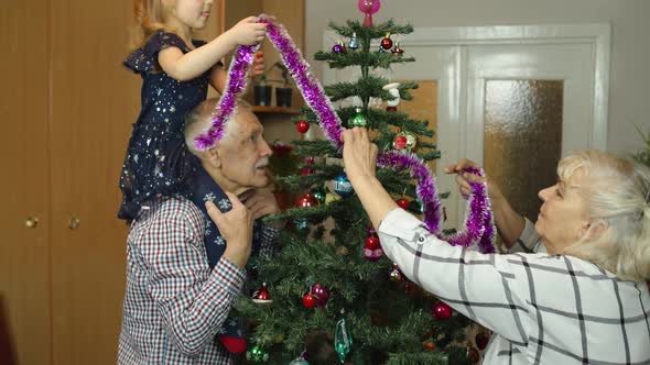 Girl Kid with Senior Grandma Grandpa Decorating Artificial Christmas Tree with Ornaments and Toys