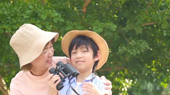 Asian Mother And Her Son Using Binocular And Pointing On Summer Day