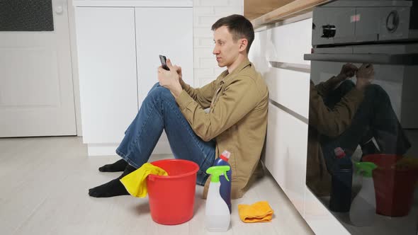 Man Takes Break After Cleaning Kitchen Using Mobile Phone