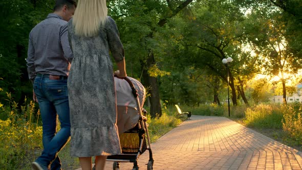 A European Couple with a Baby in a Pram Walk Along a Park Path with Beautiful Light Filtering