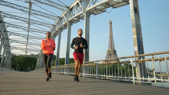 A man woman couple running across a bridge with the Eiffel Tower