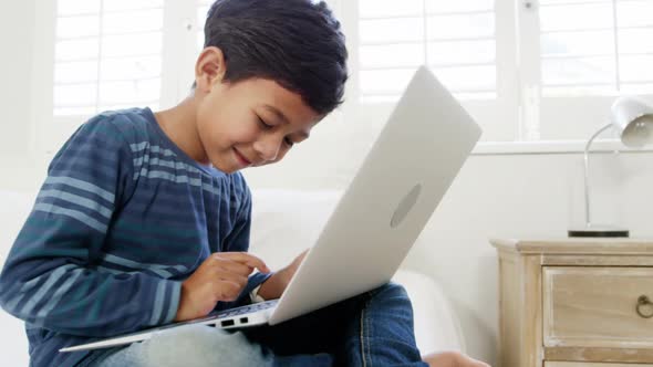 Boy using laptop while relaxing on bed