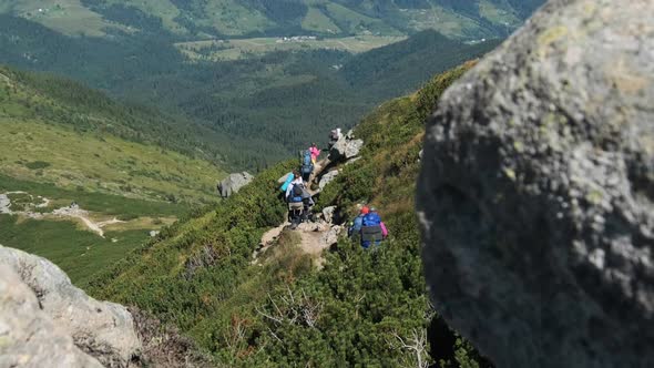 Group of Tourists and Children with Backpacks Go Down on Stone Trail in Mountain