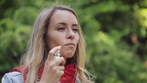 Young Woman Using Throat Spray Standing on the Park Background. Health and Medical Concept.