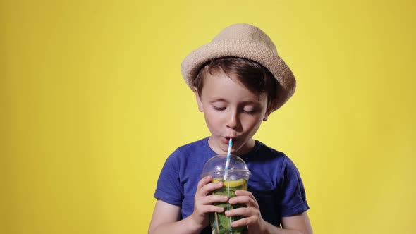 Cute boy Drinking Mojito cocktail From Plastic Cup Over Yellow Studio Backgroun