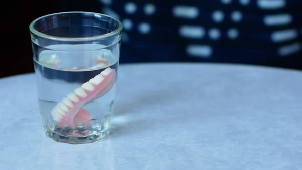 The topic is tooth loss in adulthood. Close-up glass with dentures.