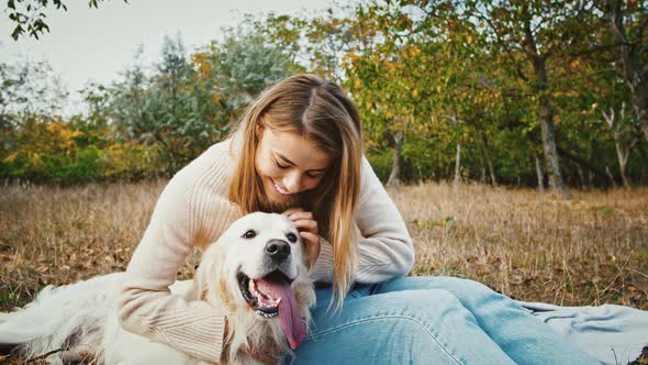 Young Charming Lady is Sitting on Blanket at Glade of Autumn Park Smiling Hugging and Stroking Her