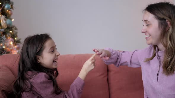 Mom and Daughter in Purple Dresses Play Chicken Cockerel Sitting on the Couch