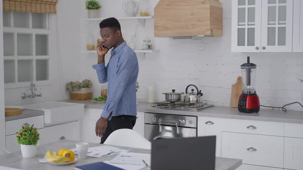 Live Camera Follows Young African American Handsome Man Walking in Kitchen Talking on Smartphone