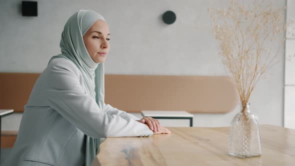 Slow Motion Portrait of Pensive Middle Eastern Woman Wearing Hijab Sitting at Table in Cafe