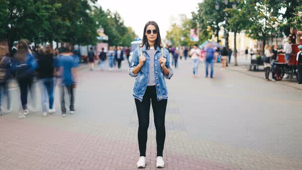 Time-lapse of Attractive Young Woman Wearing Sunglasses Standing Alone in Big City with Backpack and