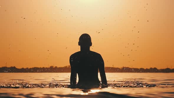 Silhouette of Young Playful Cheerful Woman Splashing River Water at Sunset