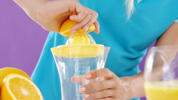 Woman preparing sweet lime juice from juicer against violet background