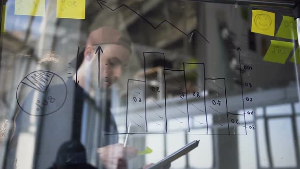 Young Attractive Hipster Man Checking Diagrams on the Glass Board