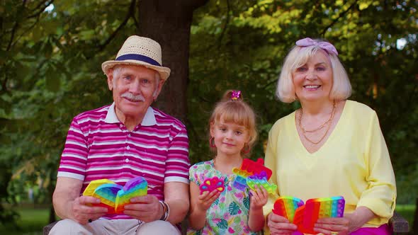 Senior Grandmother Grandfather with Granddaughter Holding Antistress Pop It Toy Games in Park