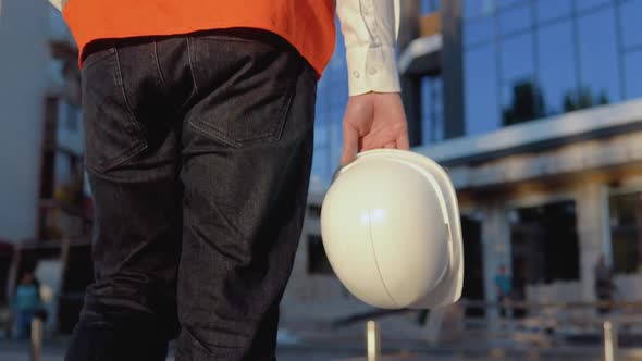 An Engineerarchitect in a White Shirt and Orange Work Vest Walks in the Direction of a Modern Glass