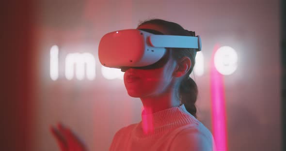 Young woman experiencing virtual reality wearing goggles with neon sign in the background