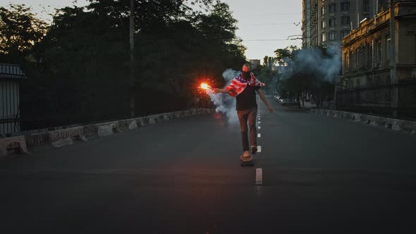 Young Fellow in Bandana on Face and Flag of USA Tied on His Chest is Riding Skateboard Along Street