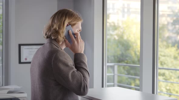 Businessman Calling By Smartphone While Standing By Office Window