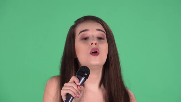 Portrait of Beautiful Young Woman Looking at Camera Sings Song Into Microphone and Dances to Music