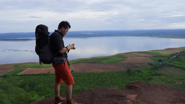 man traveler with backpack using camera taking a photo on the edge of cliff